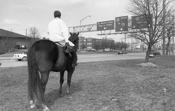 Man riding a horse, looking away from the camera at an interstate