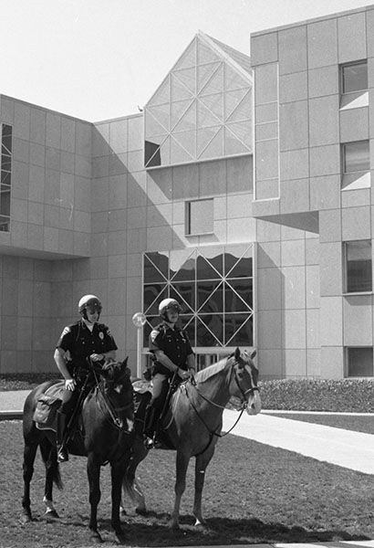 Two police officers on horses in front of the University Library building. A goose is visible on the roof