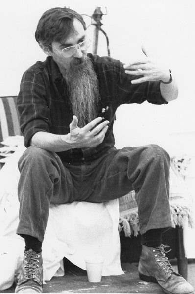 Older man with a long beard seated and gesticulating with his arms while talking
