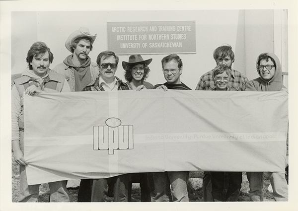 Eight students hold a banner that says 'IUPUI,' in front of a sign that reads, 'Arctic Research and Training Center'