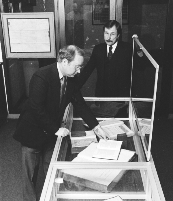 Two male university administrators place books into a glass case for display