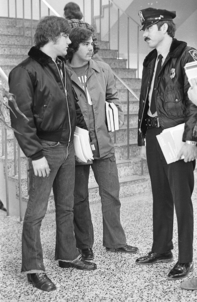 A police officer talks to two male students in front of a stair case