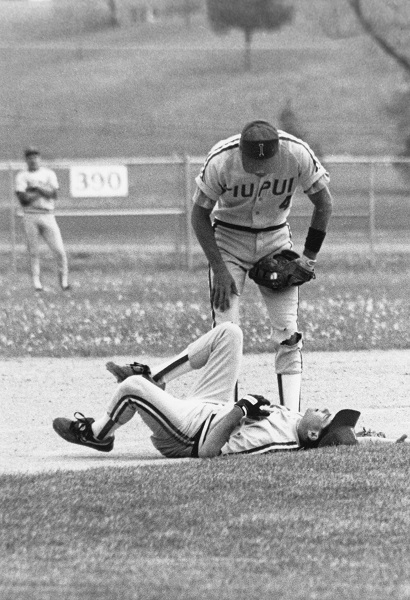 Baseball player lays on the ground, while another player stands over him looking down