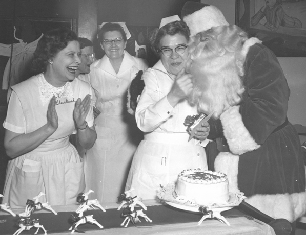 Three women in nurses uniforms smile standing next to a man dressed as Santa Clause