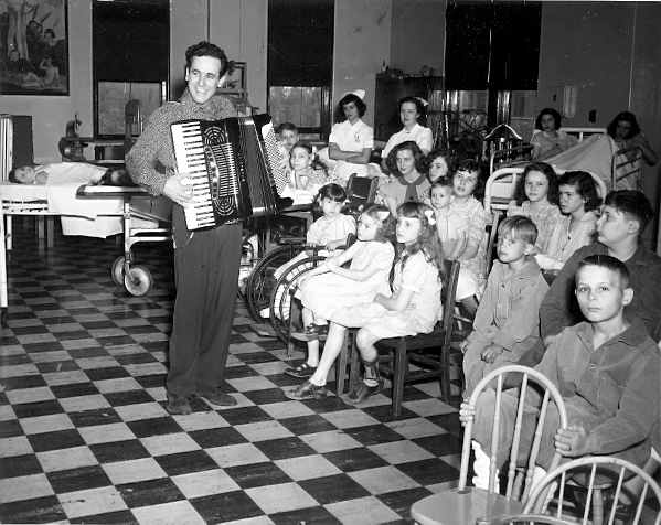 A man playing an accordian to a room full of children