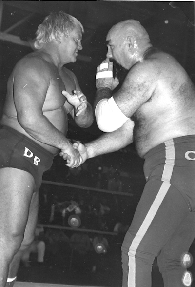 Two large men shake hands in a wrestling ring