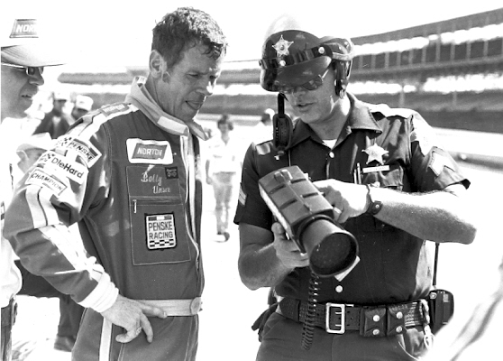 Racecar driver looks at a speedometer held by a police officer