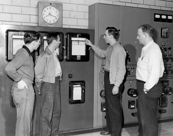 Four men look at point at a large machine taking measurments