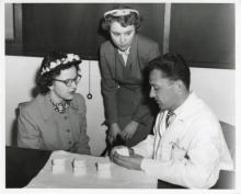 Two young women observing a man in a lab coat manipulate a dental mouth mold