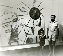Man holding a childs hand in fornt of a large abstract painting of a naked woman. The child has their finger to their lips to imply 'shush.'