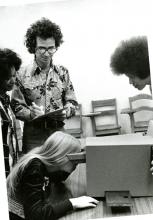 A young woman has her face to a machine, looking in, while three other people watch